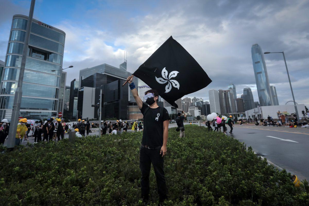 A protester waves a "Black Bauhinia" flag as others set up barricades at Lung Wo road outside the Legislative Council in Hong Kong before the flag raising ceremony to mark the 22nd anniversary of handover to China early on July 1, 2019. (Vivek Prakash/AFP/Getty Images)